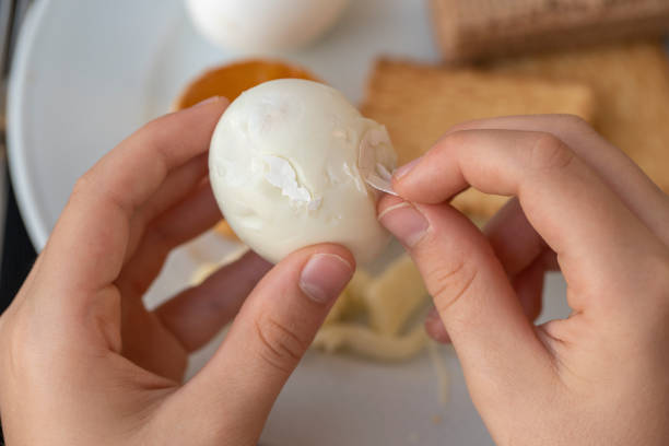 The boy is cleaning the egg with her hands, closeup. Hands peeling boiled egg.