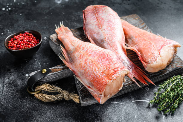 istock Whole raw red snapper fish on a cutting board.  Black background. Top view 1281297218