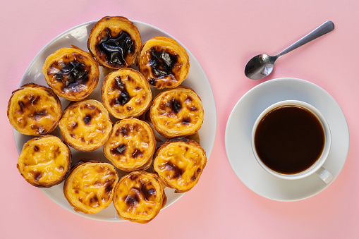 Plate of Pasteis de Belem (aslo called Portuguese Egg Tarts or Pastel de Nata) on a pink background beside a cup of coffee, Food Flat Lay