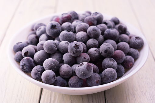 Frozen blueberries in a white plate on  a white wooden background.