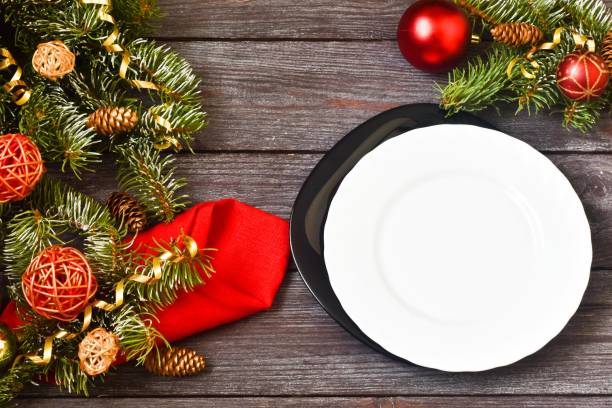 istock Christmas dinner. Christmas Day. Christmas branches with white empty plate,red napkin and cutlery on wooden background. Christmas day. New Year background. Copy space, flat lay. 1281307417