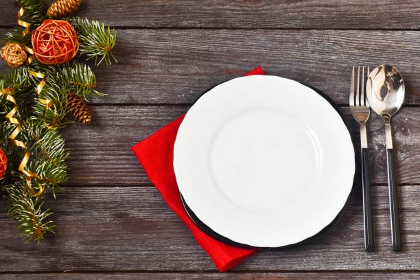 istock Christmas dinner. Christmas Day. Christmas branches with white empty plate,red napkin and cutlery on wooden background. Christmas day. New Year background. Copy space, flat lay. 1281307437