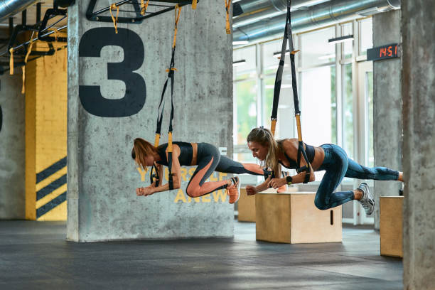 Two young athletic girls exercising with trx fitness straps at gym Two young athletic girls exercising with trx fitness straps at gym. Sport, partner workout, wellness and healthy lifestyle suspension training stock pictures, royalty-free photos & images