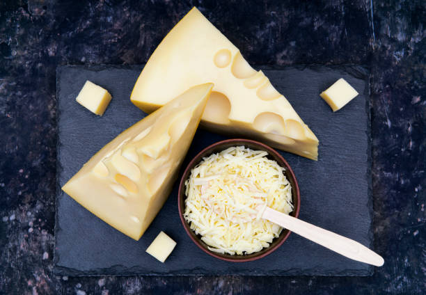 duas cunhas de queijo e uma tigela de queijo ralado em uma tábua de pedra preta - food and drink cheese grated bowl - fotografias e filmes do acervo