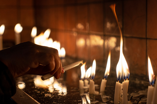 Woman lights candle in glass holder with wooden skewer on green background closeup. Candlelight creating cozy atmosphere at home. Copy space