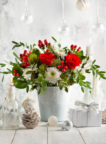 Christmas or New Year concept. Festive winter flower arrangement with red roses, white chrysanthemum and berries in vase on table decorated for holiday. Christmas or New Year concept. rose bouquet red table stock pictures, royalty-free photos & images