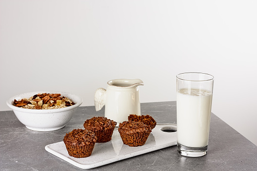 Healthy breakfast. Carrot vegan muffins, muesli or granola on white bowl and glass of milk on gray stone table. Kinfolk style.