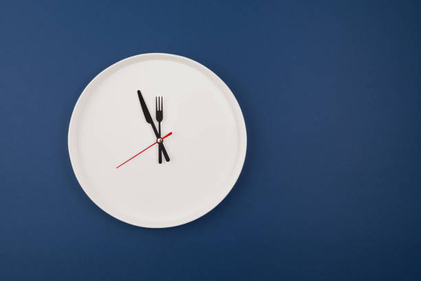 복사 공간이있는 파란색 배경의 흰색 플레이트 시계. 손은 12시를 가리킵니다. 간격 금식 또는 자동 phagy - 12 oclock 뉴스 사진 이미지