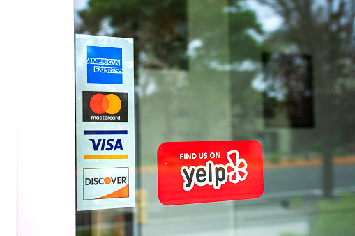 MasterCard, VISA, American Express, Discover payment options advertised on a restaurant door. A red sticker decal promotes Yelp crowd-sourced reviews service - San Francisco, California, USA - 2020