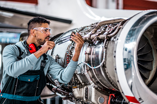 Aircraft Maintenance Mechanic Inspecting and Working on Airplane Jet Engine in the Hangar.