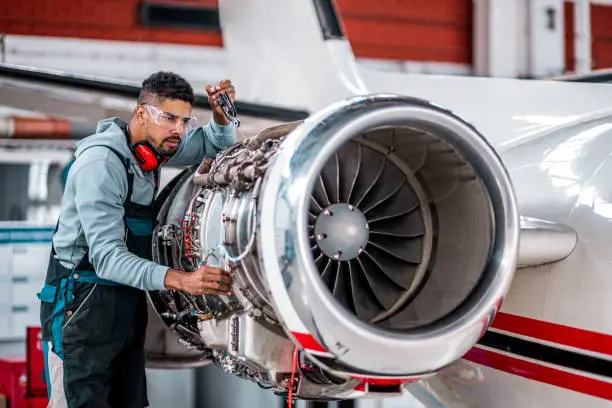 Aircraft mechanic inspecting and checking the technology of a jet engine in the hangar at the airport.