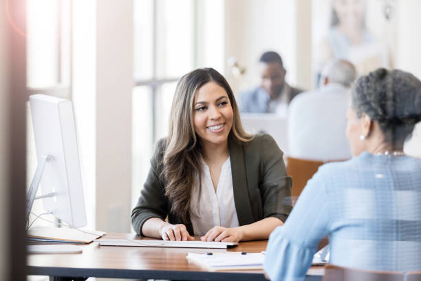 Bank employee assisting female customer A friendly bank employee assists a mature female customer with opening a bank account. The bank employee is using a computer to input the customer's information. types of loans stock pictures, royalty-free photos & images