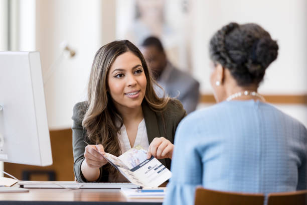 Bank employee explains bank services to new customer A cheerful female banker explains the different types of banking accounts to a new customer. The banker is showing the customer an informational brochure. bank account photos stock pictures, royalty-free photos & images