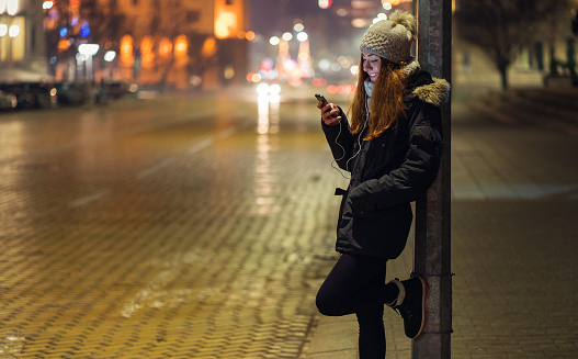 Young woman browsing on her mobile phone while waiting on the street