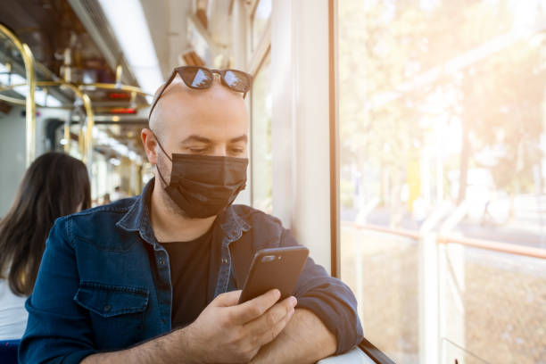 A young man in a black mask looking at his smartphone while traveling on the subway. stock photo