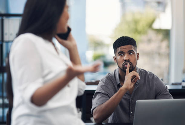 A noisy coworker can derail your productivity Shot of a young businessman gesturing for his colleague to be quiet in an office finger on lips stock pictures, royalty-free photos & images