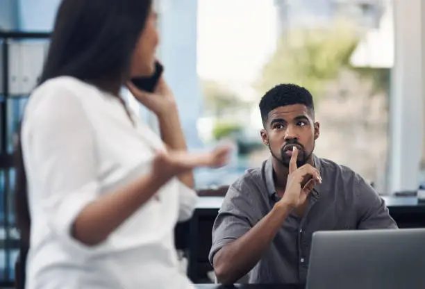 Shot of a young businessman gesturing for his colleague to be quiet in an office