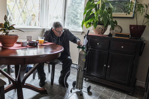 In order to make sure the settings are correct, a senior man is checking his portable oxygen tank before having breakfast. Real life photography. oxygen cylinder stock pictures, royalty-free photos & images