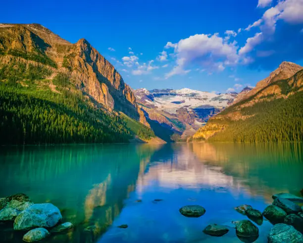 EARLY MORNING CALM WATERS OF LAKE LOUISE REFLECTS THE CANADIAN ROCKIES