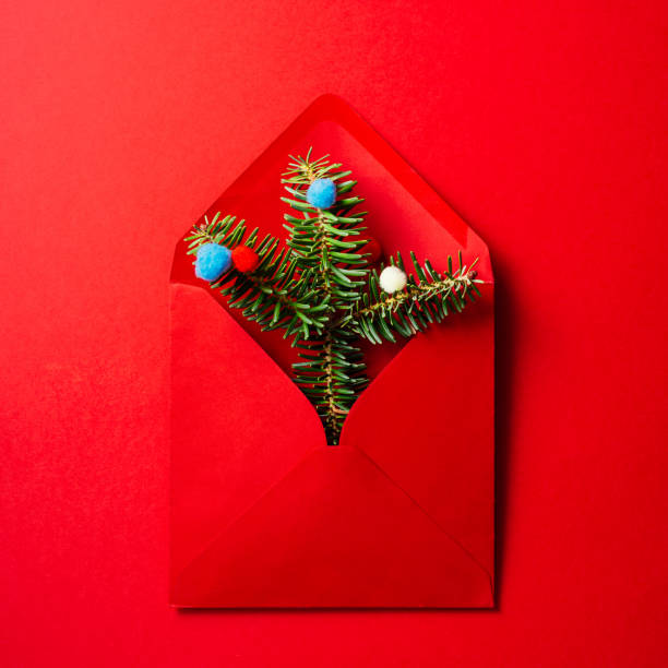 istock Christmas composition. Red envelope with fir branches and pastel colored wool balls on red  background. 1281348827
