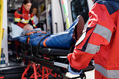 Selective focus of paramedic in uniform carrying stretcher with patient in ambulance ca outdoors