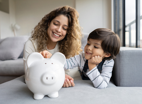 Portrait of a happy Latin American single-parent-family saving money in a piggybank - home finances concepts