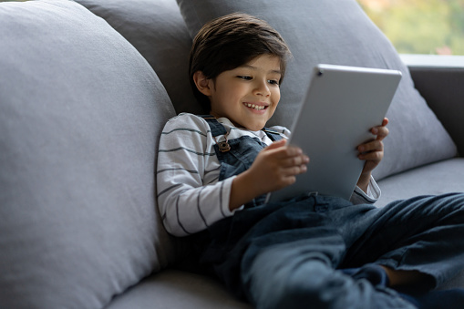 Portrait of a happy boy watching videos online on a digital tablet at home and smiling - lifestyle concepts