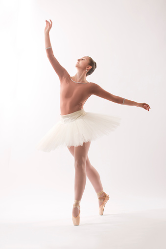 Young woman ballet dancer in pointe shoes and white tutu with pink top, dancing in the studio against a white background.