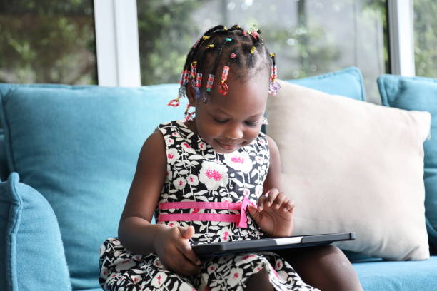 African American kid is homeschooling by learning from digital tablet while sitting on sofa couch