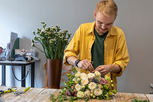 A male florist decorates a flower bouquet in a flower salon.