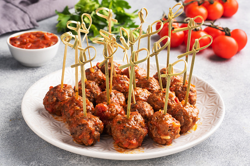 Beef meatballs stewed in tomato sauce on a plate on barbecue skewers. Light concrete background