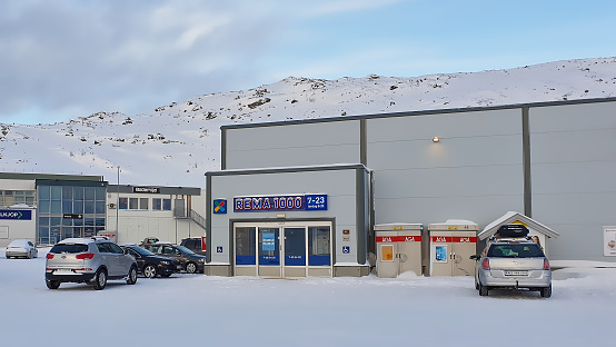 Hammerfest, Norway - 03/01/2019: Cars on snow-covered parking lot in front of the Norwegian food discounter Rema 1000 in Hammerfest during winter time.