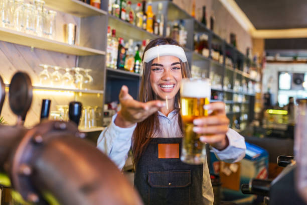 istock Bartender with face shield covid-19 protection, serving a draft beer at the bar counter during coronavirus pandemic, shelves full of bottles with alcohol on the background 1281392748