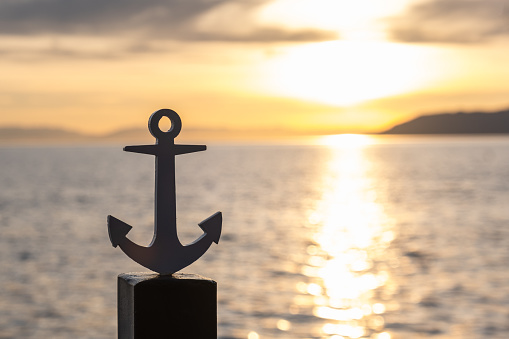 Silhouette of the stylized anchor of the ship on the landing, against the background of sunset. The concept of sea travel, adventure. Copy space.