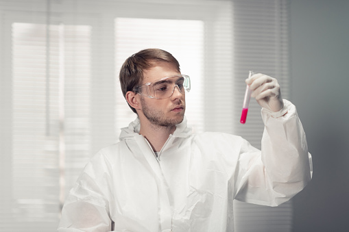 A portrait of a young scientist in protective goggles holding a test tube with a red liquid.