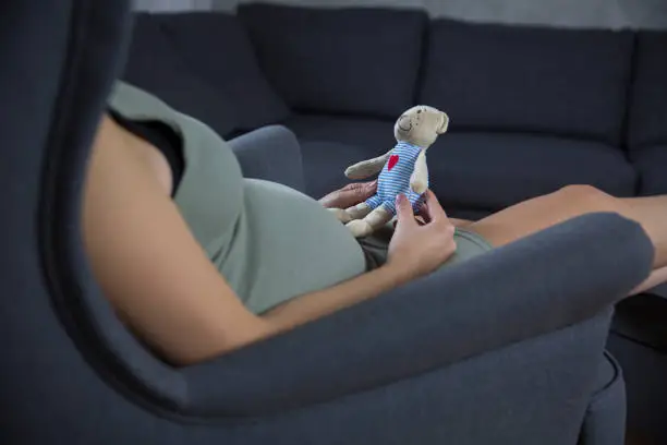 Pregnant woman seat on armchair holding a toy for hear child. Woman waiting for the childbirth.