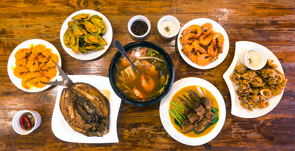 Top view of Filipino cuisine on a wood table at a local restaurant. Included in photo - Pork belly in peanut sauce, shrimps, sinigang na hipon, bangus, and mussels.