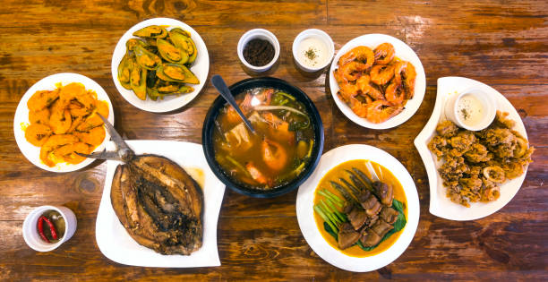 Top view of Filipino cuisine on a wood table at a local restaurant. Included in photo - Pork belly in peanut sauce, shrimps, sinigang na hipon, bangus, and mussels. Top view of Filipino cuisine on a wood table at a local restaurant. Included in photo - Pork belly in peanut sauce, shrimps, sinigang na hipon, bangus, and mussels. filipino restaurant stock pictures, royalty-free photos & images