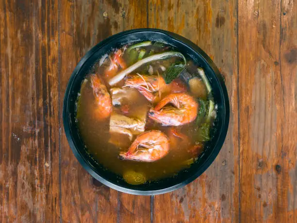 Photo of Sinigang na Hipon is a type of Filipino sour tamarind soup. Top view, on a wood table.