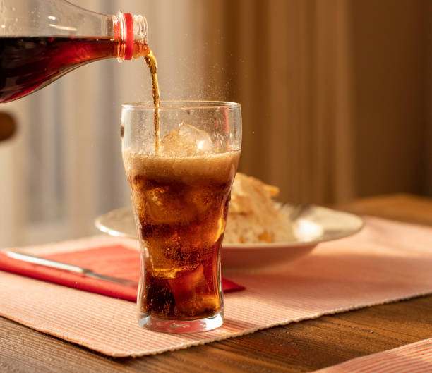 gießen cola aus flasche in glas und fizz mit eiswürfeln auf dem tisch gegen verschwommenen livinroom hintergrund - säure stock-fotos und bilder