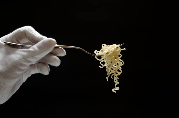 Silver fork and just cooked noodles on it against dark background.Empty space