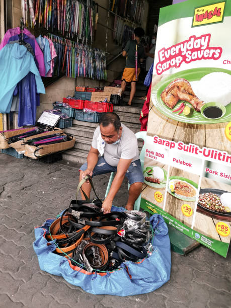 Divisoria, Manila, Philippines - A male peddler sells belts beside a fastfood advertisement. Shot along Recto Avenue. Divisoria, Manila, Philippines - Oct 2020: A male peddler sells belts beside a fastfood advertisement. Shot along Recto Avenue. divisoria market stock pictures, royalty-free photos & images