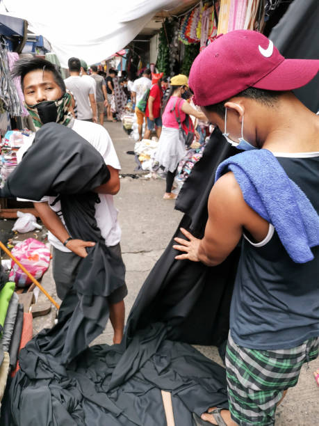 Divisoria, Manila, Philippines - Two vendors fold black fabric that is about to be bought by a customer Divisoria, Manila, Philippines - Oct 2020: Two vendors fold black fabric that is about to be bought by a customer divisoria market stock pictures, royalty-free photos & images