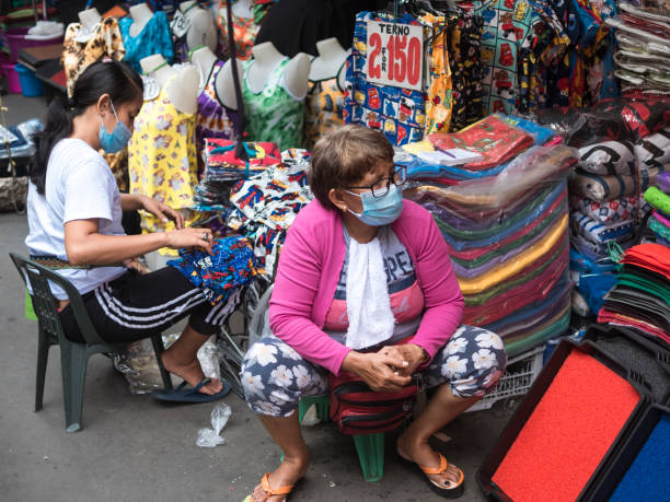 Divisoria, Manila, Philippines - A middle aged female vendor and her assistant sells clothes at a street market. Divisoria, Manila, Philippines - Oct 2020: A middle aged female vendor and her assistant sells clothes at a street market. divisoria market stock pictures, royalty-free photos & images