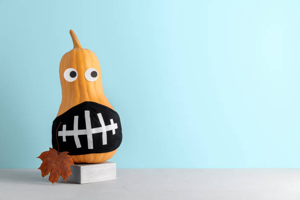 istock Funny pumpkin with face protective mask on pastel blue background with copy space. 1281415290