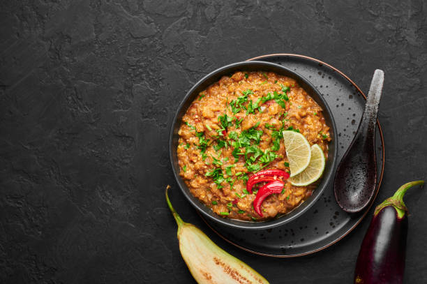 istock Baingan Bharta or Roasted Mashed Eggplant in black bowl on dark slate table top. Bhurta is indian cuisine puree dish of fire roasted eggplant and masala. Top view. Copy space 1281422085
