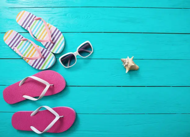 Photo of Flip flops, sunglasses and sea shell on blue wooden background. Copy space and fashion summer accessories.