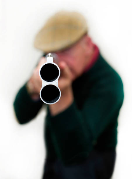 Staring down the barrel of an 'Over and Under' double barreled shotgun head-on, pointing straight at the camera with a sportsman wearing country style clothing and cloth cap