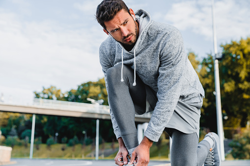 Thoughtful good-looking sportsman tying shoelaces on his sneakers getting ready for jogging outside