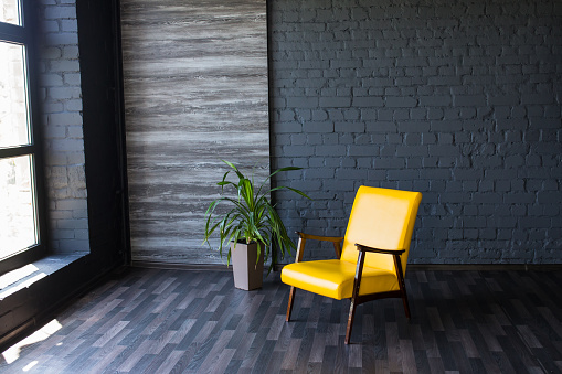 Stylish retro yellow chair in the gray room. Brick gray wall.